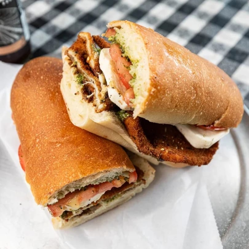 Two halves of a crispy chicken cutlet sandwich with fresh mozzarella, tomato, and pesto.