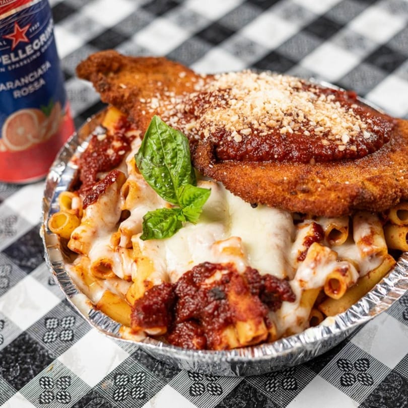 Chicken parmesan over pasta with melted cheese and sauce, garnished with basil, next to a soda can.