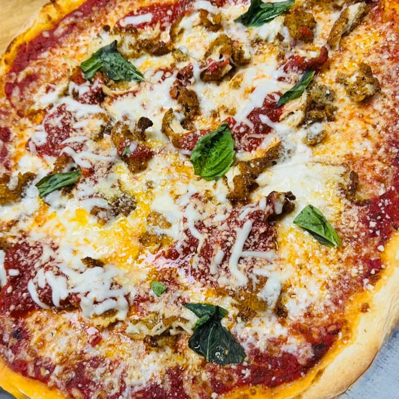 Close-up of a Seneca's Italian Deli & Market pizza with tomato sauce, melted cheese, sausage, and basil.