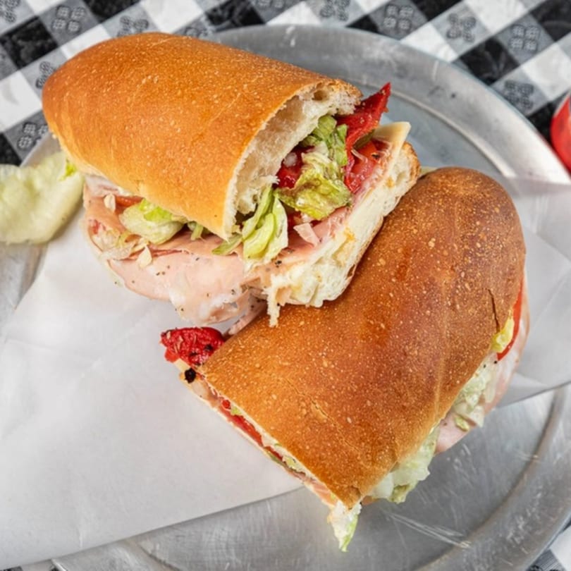 A large Italian deli sub, sliced in half, filled with meats, cheese, lettuce, and red peppers.