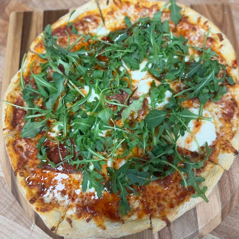 A freshly baked pizza from Seneca's Italian Deli & Market, topped with arugula and balsamic glaze.